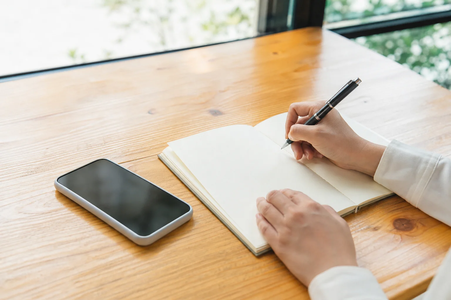既卒のフリーターが就活の準備として、机の上でノートに卒業後の経歴を書き出している手元